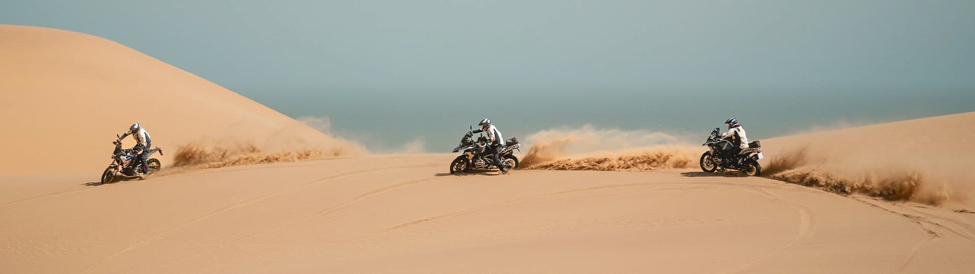 Vediamo tre moto BMW sfrecciare su una duna sabbiosa.